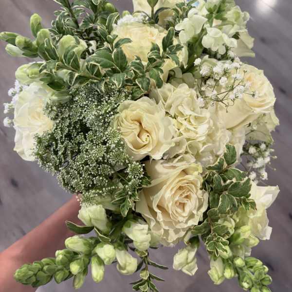 Cream roses and white flowers in a hand-held bouquet with variegated greenery.