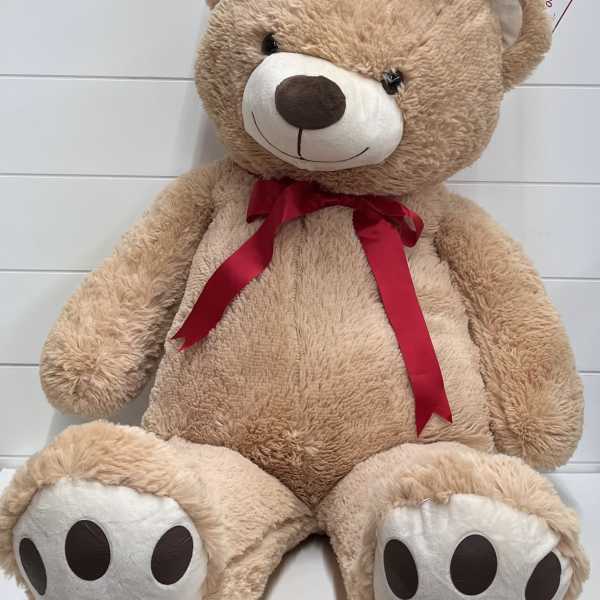 Large tan teddy bear with a red ribbon bow