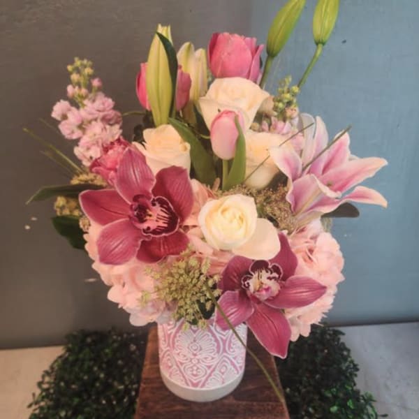 Pink and white mixed flower arrangement with orchids, roses, lilies, and tulips in a patterned vase.