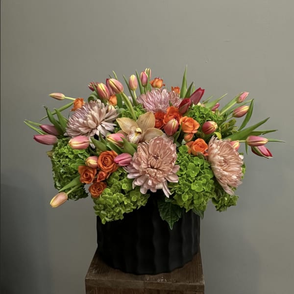Mixed bouquet of pink tulips, orange roses, and pale chrysanthemums in a black container