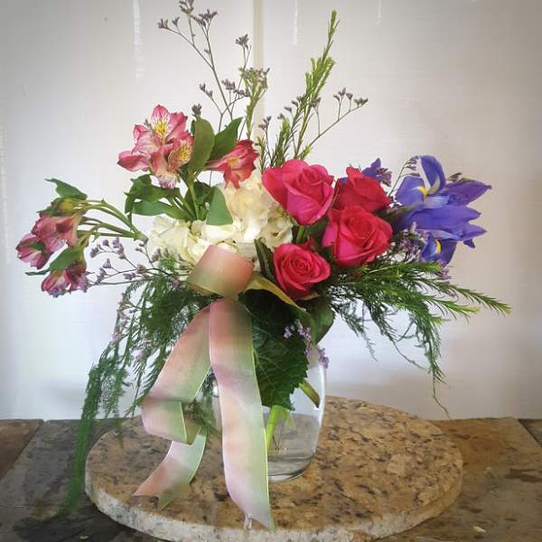 Mixed bouquet of roses, alstroemeria, and irises in a glass vase with ribbon