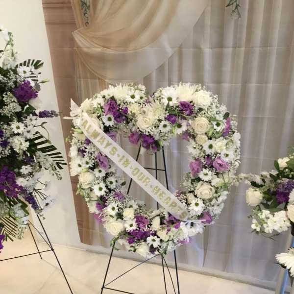 Heart-shaped floral wreath on a stand with white and purple flowers