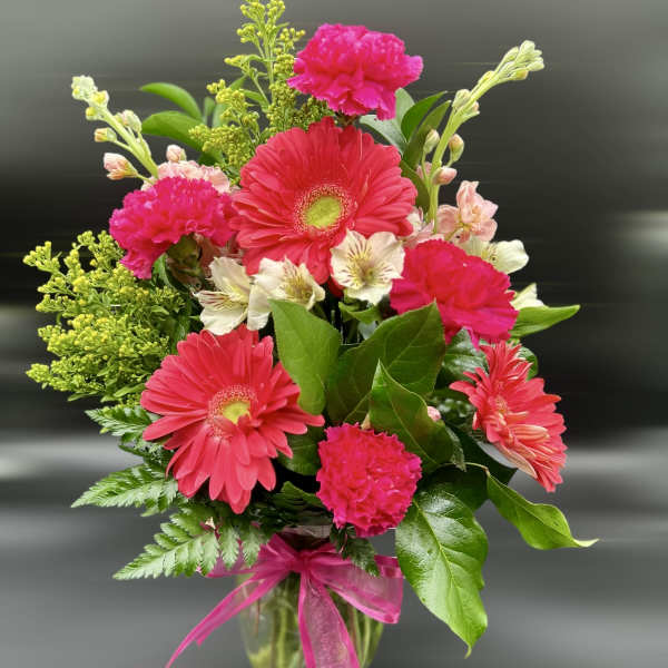 Bright pink gerbera daisies, carnations, and light alstroemeria in a clear vase with pink bow