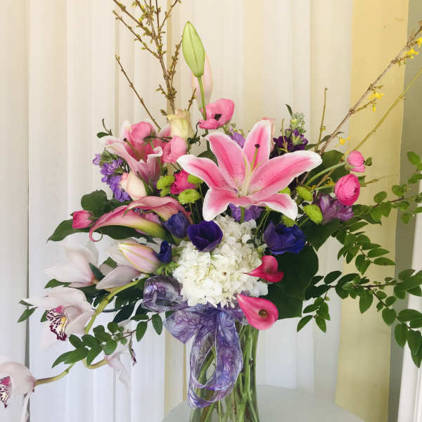 Pink lilies and mixed flowers in a glass vase with a purple ribbon