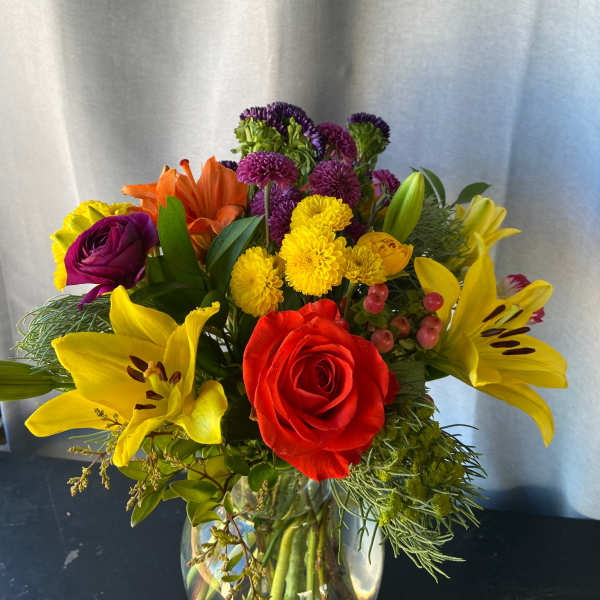 Colorful mixed bouquet in a clear glass vase with roses, lilies, and chrysanthemums