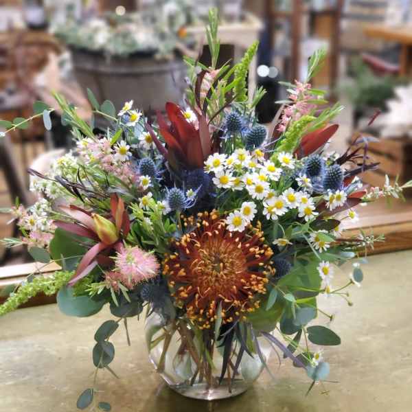 Mixed bouquet in a clear glass vase with daisies and spiky blue flowers