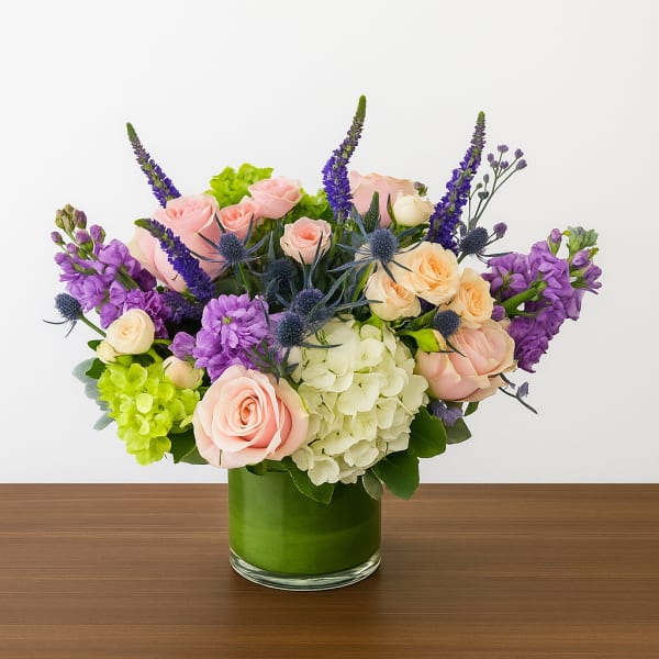 Bouquet of pink and cream roses with purple flowers in a green glass vase