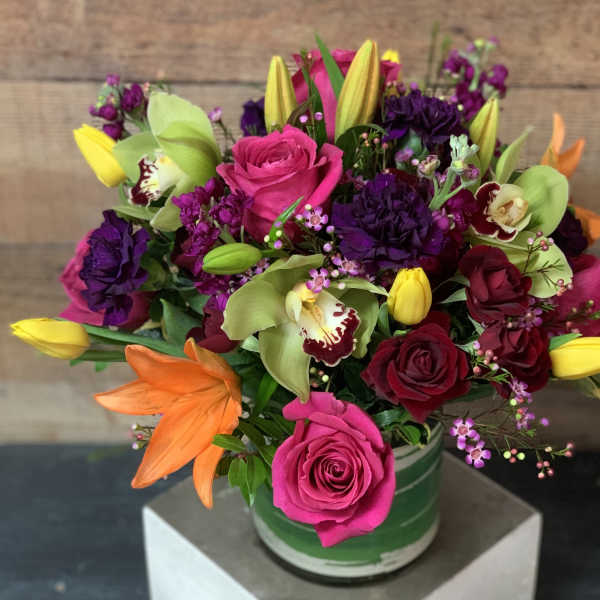 Bright mixed bouquet with roses, tulips, orchids, and lilies in a green vase