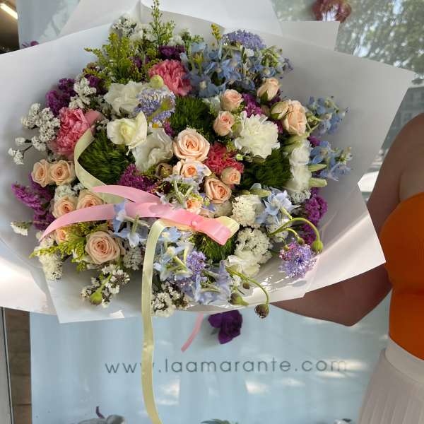 Mixed bouquet of pastel roses, carnations, and blue flowers wrapped in white paper