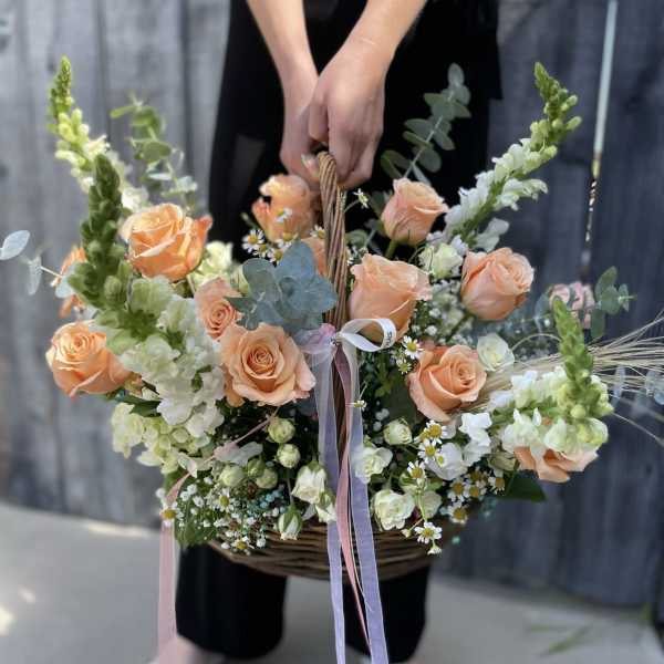 Large peach rose and white flower basket arrangement with long pastel ribbons
