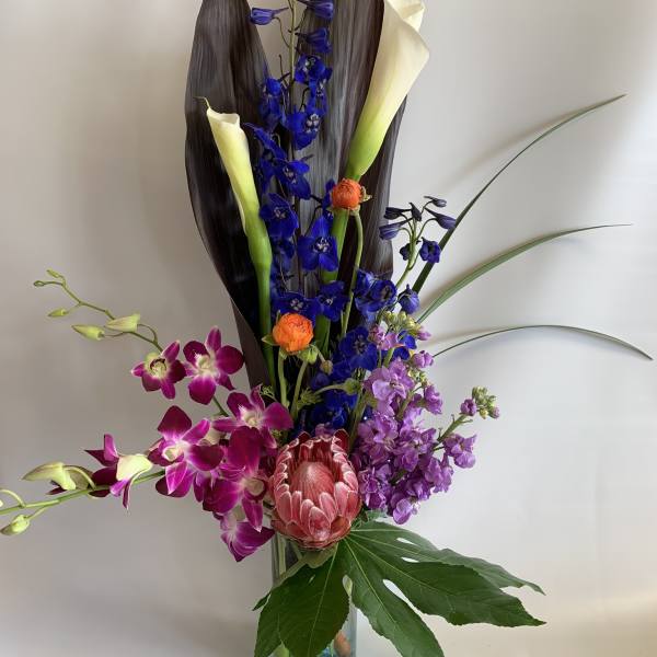 Tall mixed bouquet with blue, purple, and white blooms in a glass vase