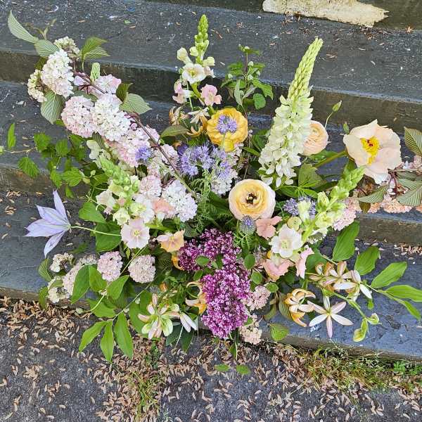 Loose garden-style arrangement of pastel flowers with purple accents displayed on outdoor stone steps