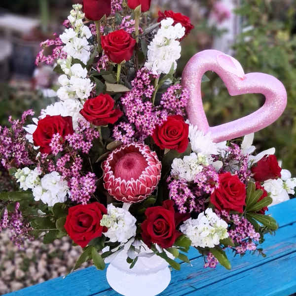 Red roses and white blooms in a vase with a pink heart pick