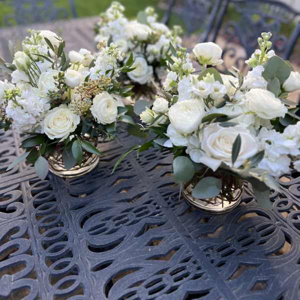 White floral centerpieces in low gold containers on an outdoor table