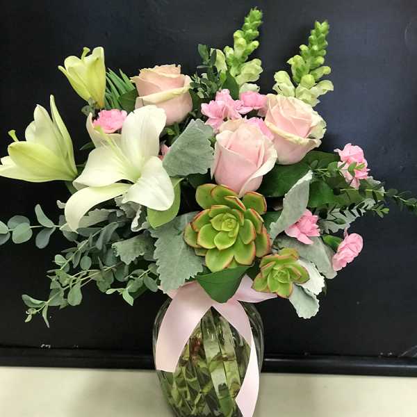 Pink roses and white lilies arranged in a glass vase with succulents.