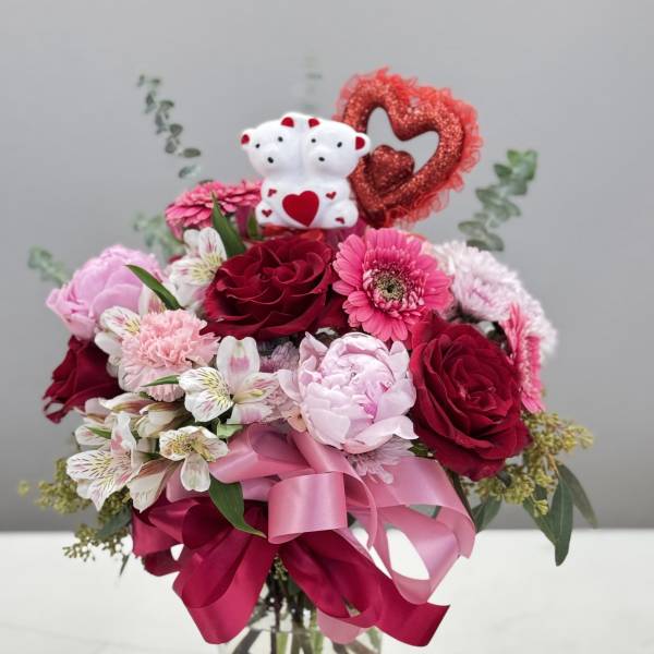 Pink and red bouquet in a glass vase with teddy bears and a heart decoration