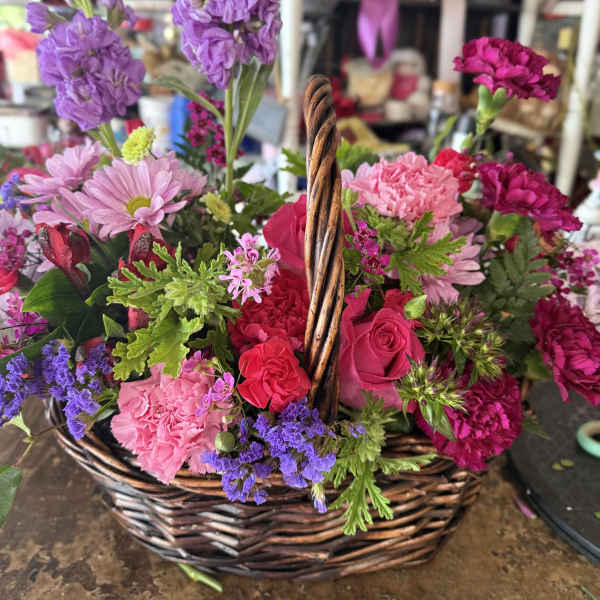 Basket of pink, purple, and red flowers with a woven handle