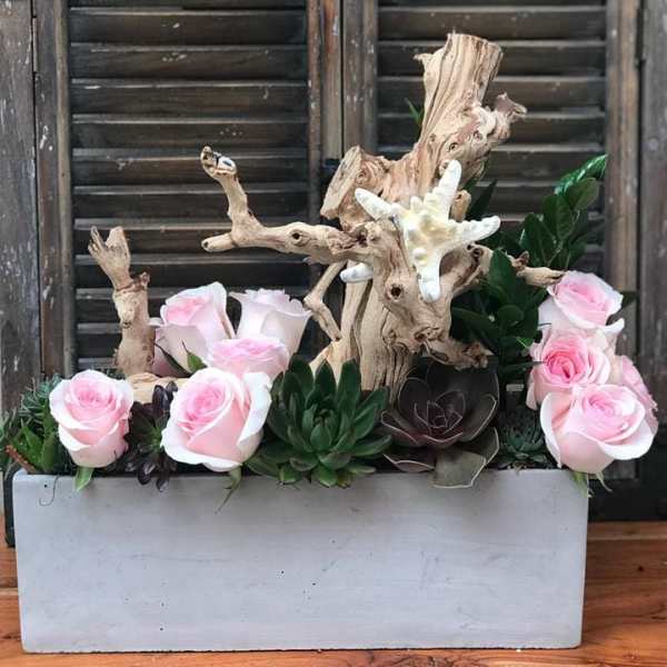 Pink roses and succulents arranged with driftwood in a white planter