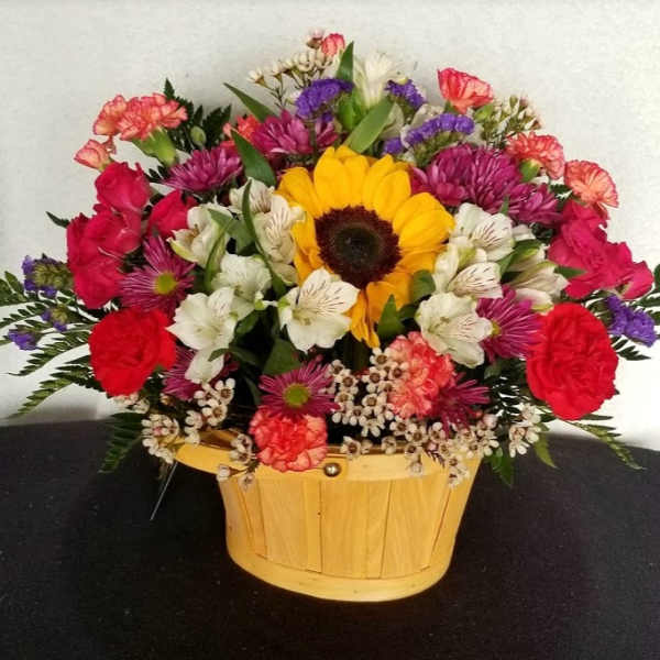 Mixed bouquet in a wooden basket with a sunflower, roses, and white blooms
