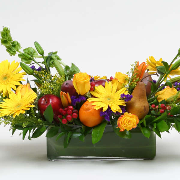 Yellow daisies and fruit arranged in a rectangular glass vase