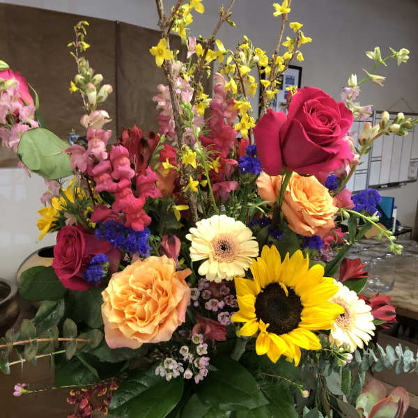 Colorful mixed bouquet in a tall green vase with roses and sunflowers