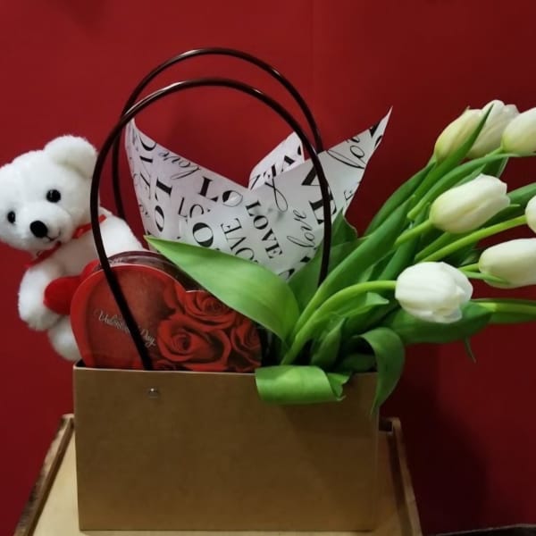 White tulips in a gift bag with a teddy bear and heart-shaped box