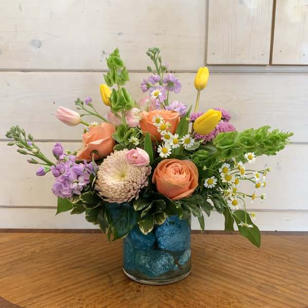 Mixed bouquet in a blue glass vase with peach, yellow, and lavender flowers