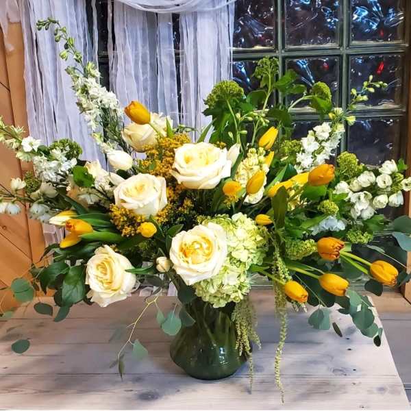 White roses and yellow tulips in a green glass vase