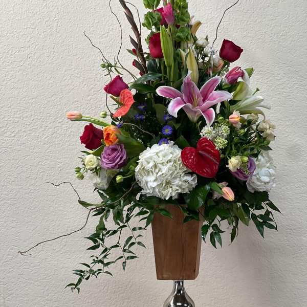Tall mixed flower arrangement in a wooden vase with pink lilies and red roses