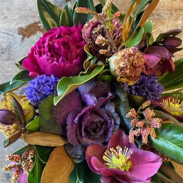 Purple and magenta floral bouquet with mixed blooms and broad leaves