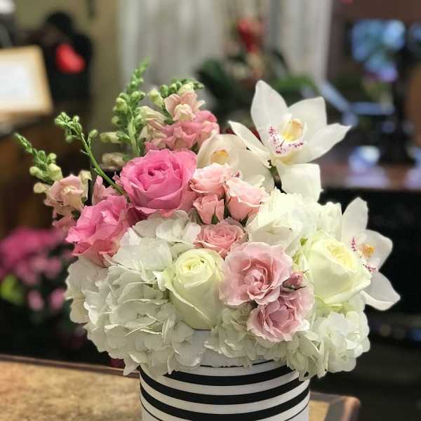 Pink and white roses with white orchids in a striped hat box