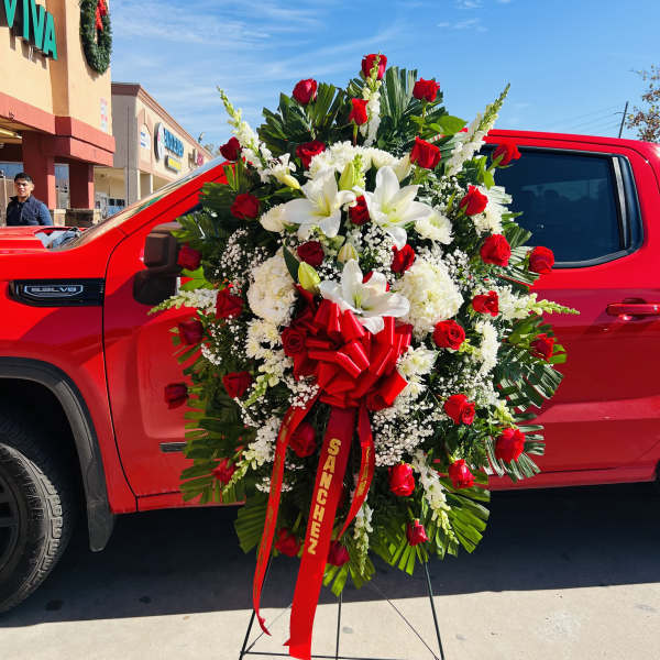 Tall standing spray of red roses and white lilies with a large red memorial ribbon
