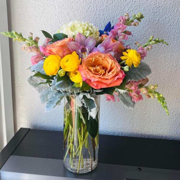 Mixed bouquet of roses, orchids, and yellow blooms in a glass vase