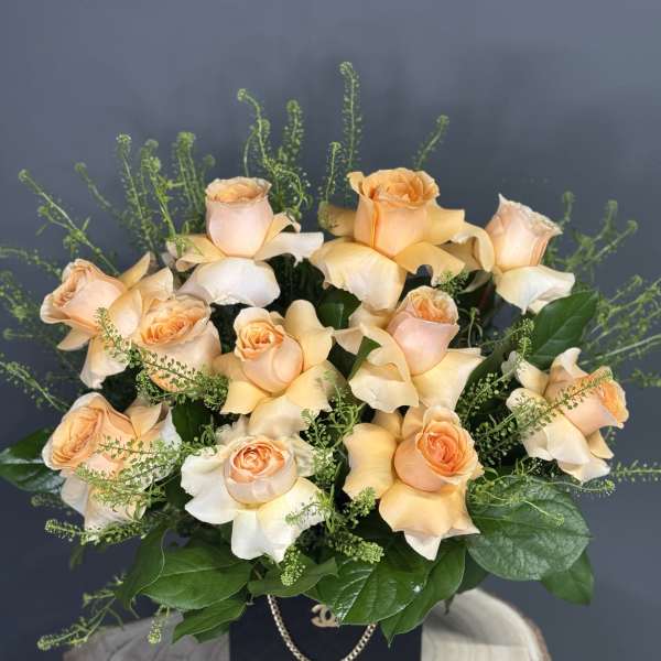 Peach roses arranged in a black box with greenery