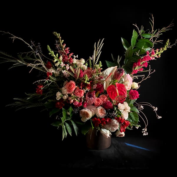 Large floral arrangement with pink and red blooms in a dark vase