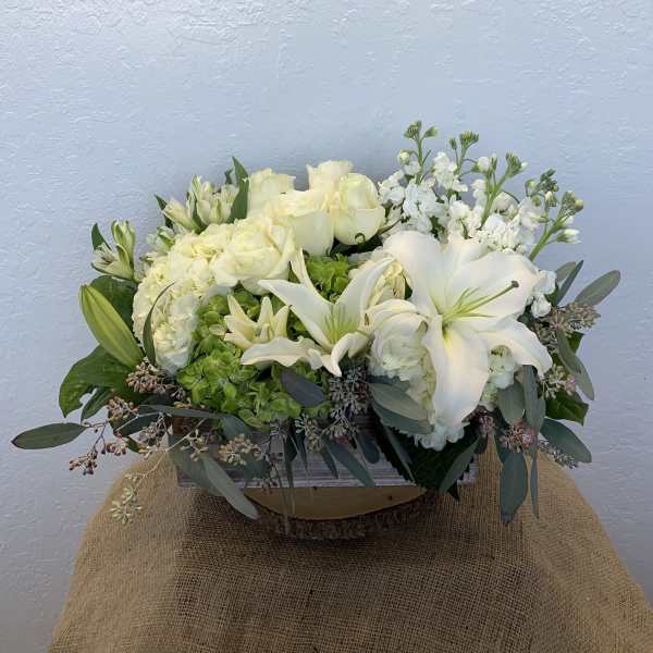 White floral arrangement with lilies, roses, and hydrangeas in a wooden container