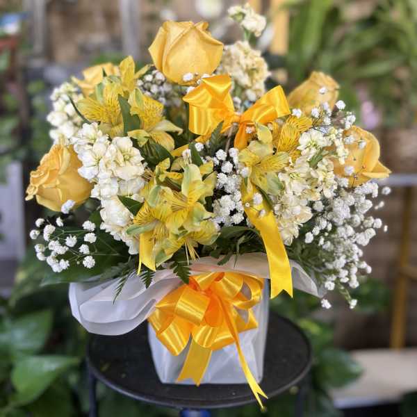 Yellow roses and white flowers in a wrapped gift arrangement with ribbon
