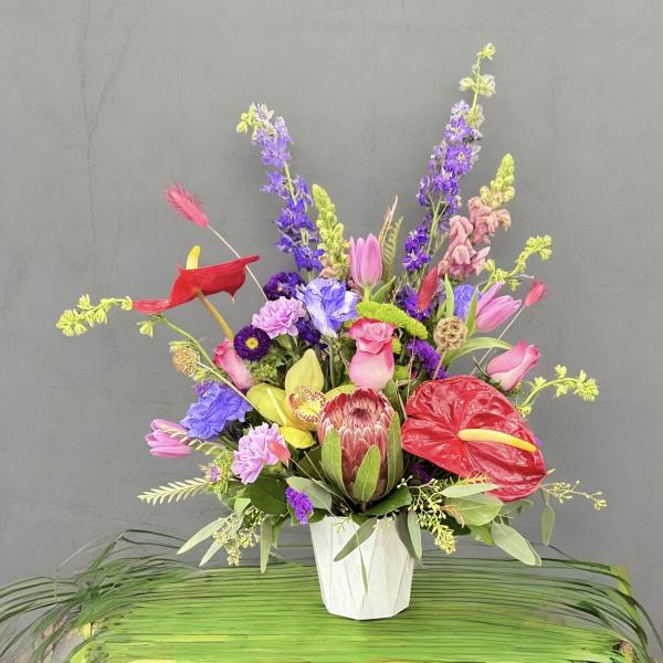 Colorful mixed bouquet in a white vase with anthuriums and tall purple blooms