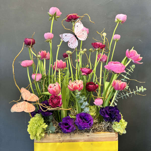 Tall pink and purple floral arrangement in a wooden box with butterflies