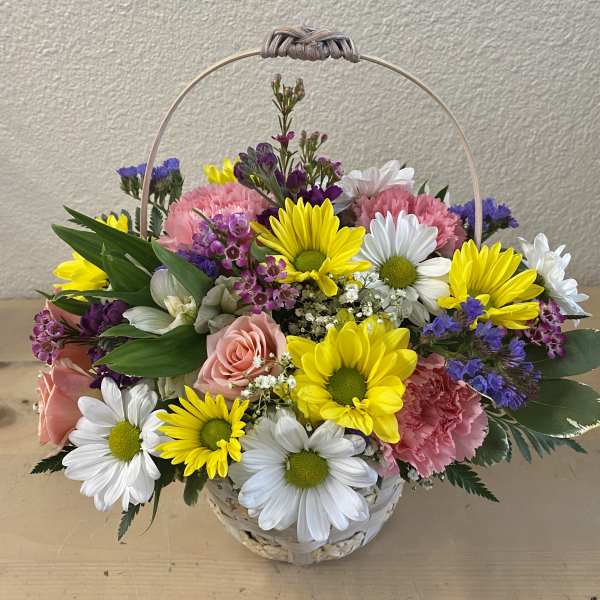 Basket arrangement of daisies, roses, and carnations in pink, yellow, white, and purple