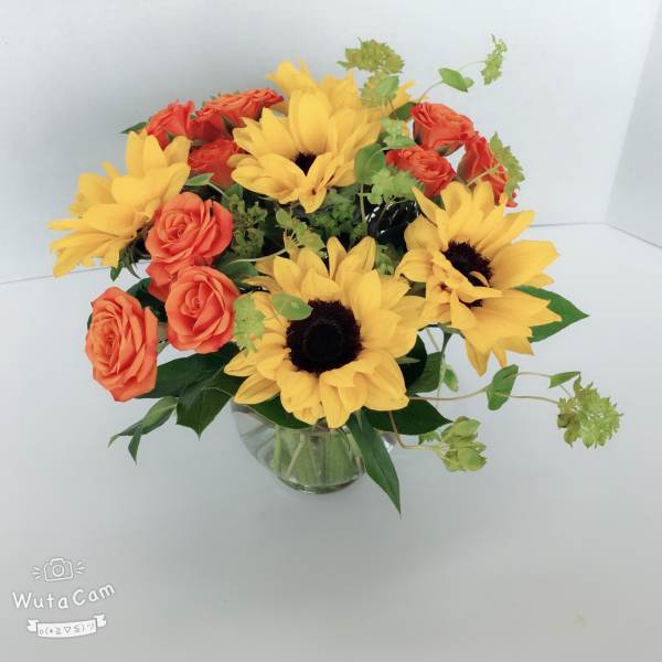 Bouquet of yellow sunflowers and orange roses in a glass vase