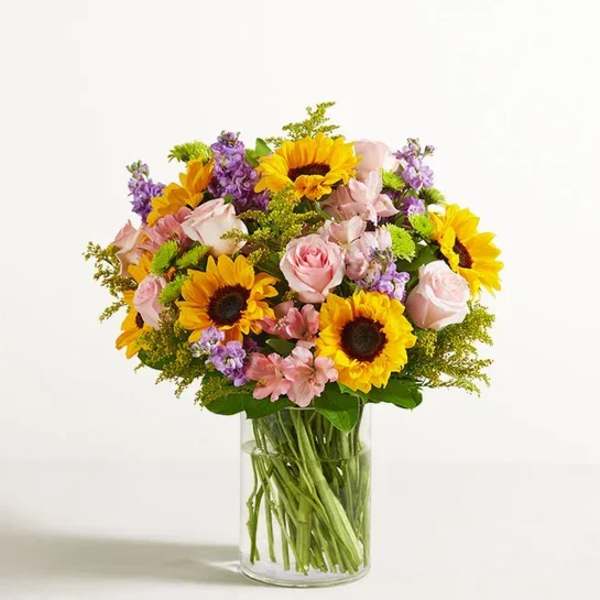 Bouquet of sunflowers, pink roses, and purple flowers in a glass vase
