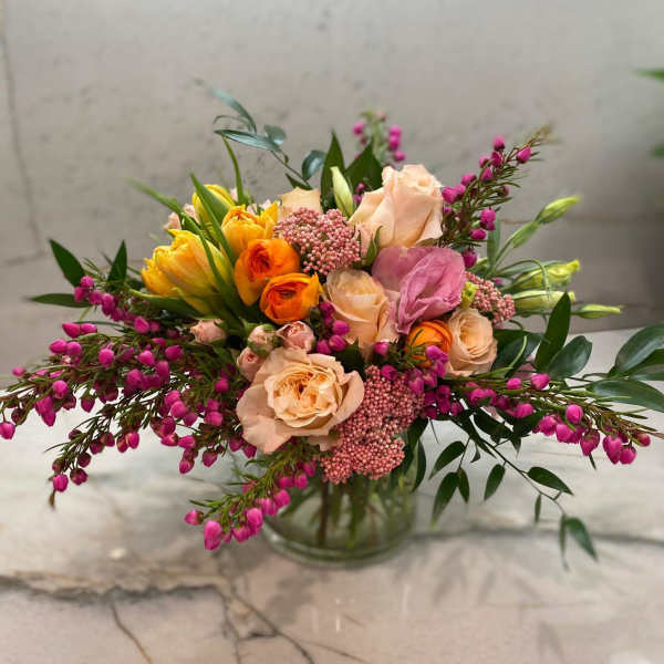 Mixed bouquet of peach, pink, and yellow flowers in a glass vase