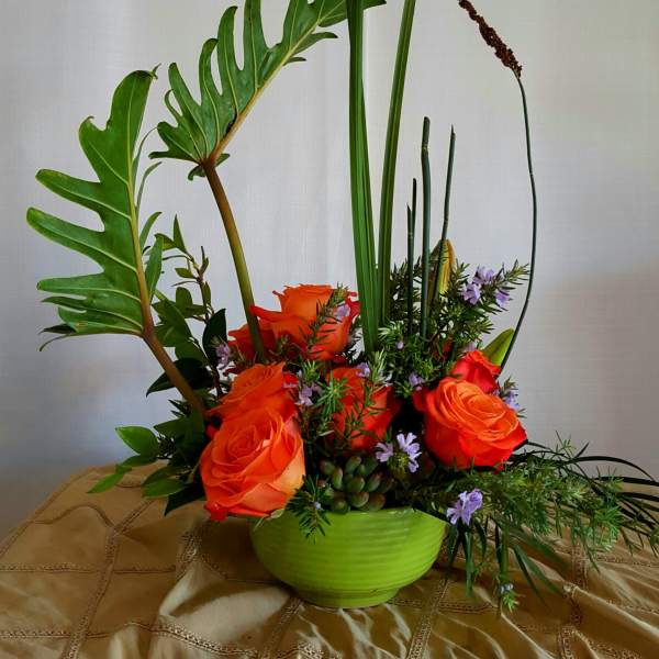 Orange roses in a green bowl with tall tropical leaves