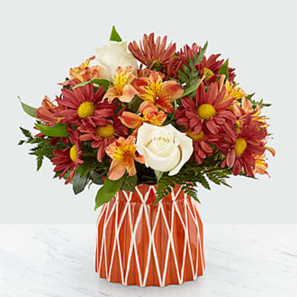 Bouquet of red daisies, white roses, and orange alstroemeria in a patterned vase