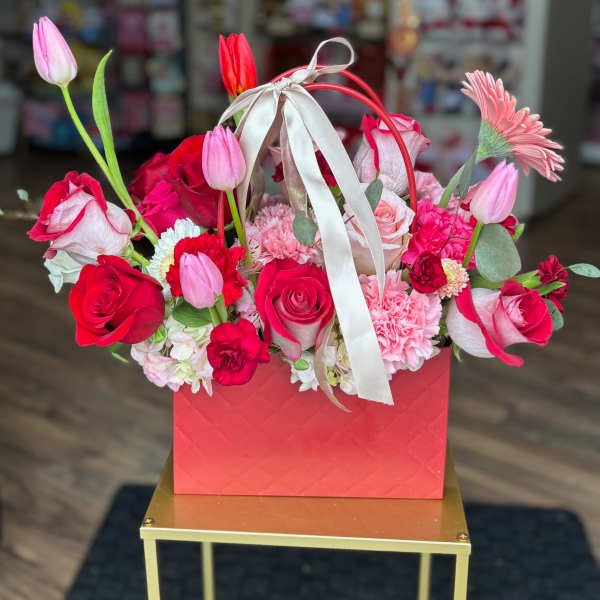 Pink and red flower arrangement in a red gift box with a ribbon handle