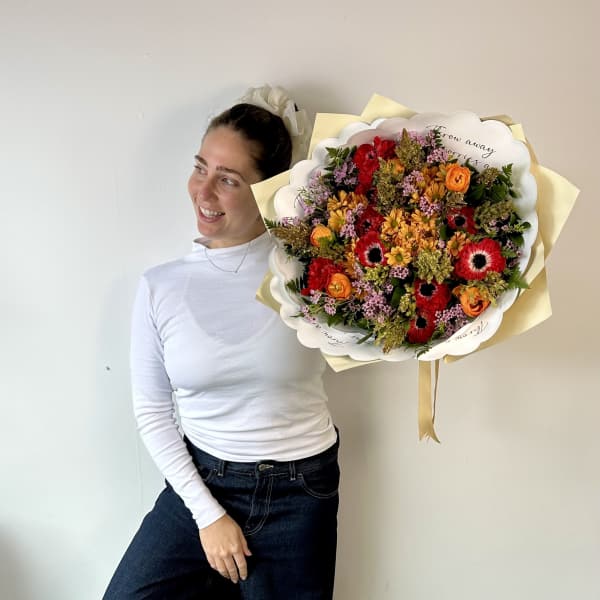 Woman holding a large mixed bouquet of red, orange, and pink flowers