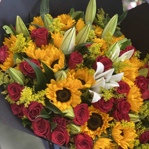 Bouquet of red roses, sunflowers, and white lilies wrapped in black paper