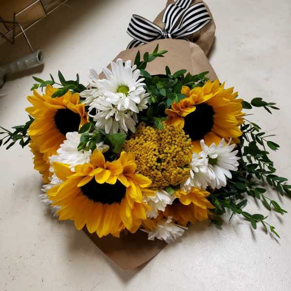 Bouquet of sunflowers, white daisies, and yellow filler flowers wrapped in brown paper