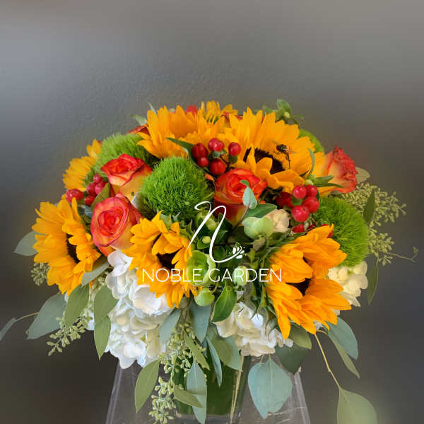 Bouquet of sunflowers, orange roses, and white hydrangeas in a glass vase